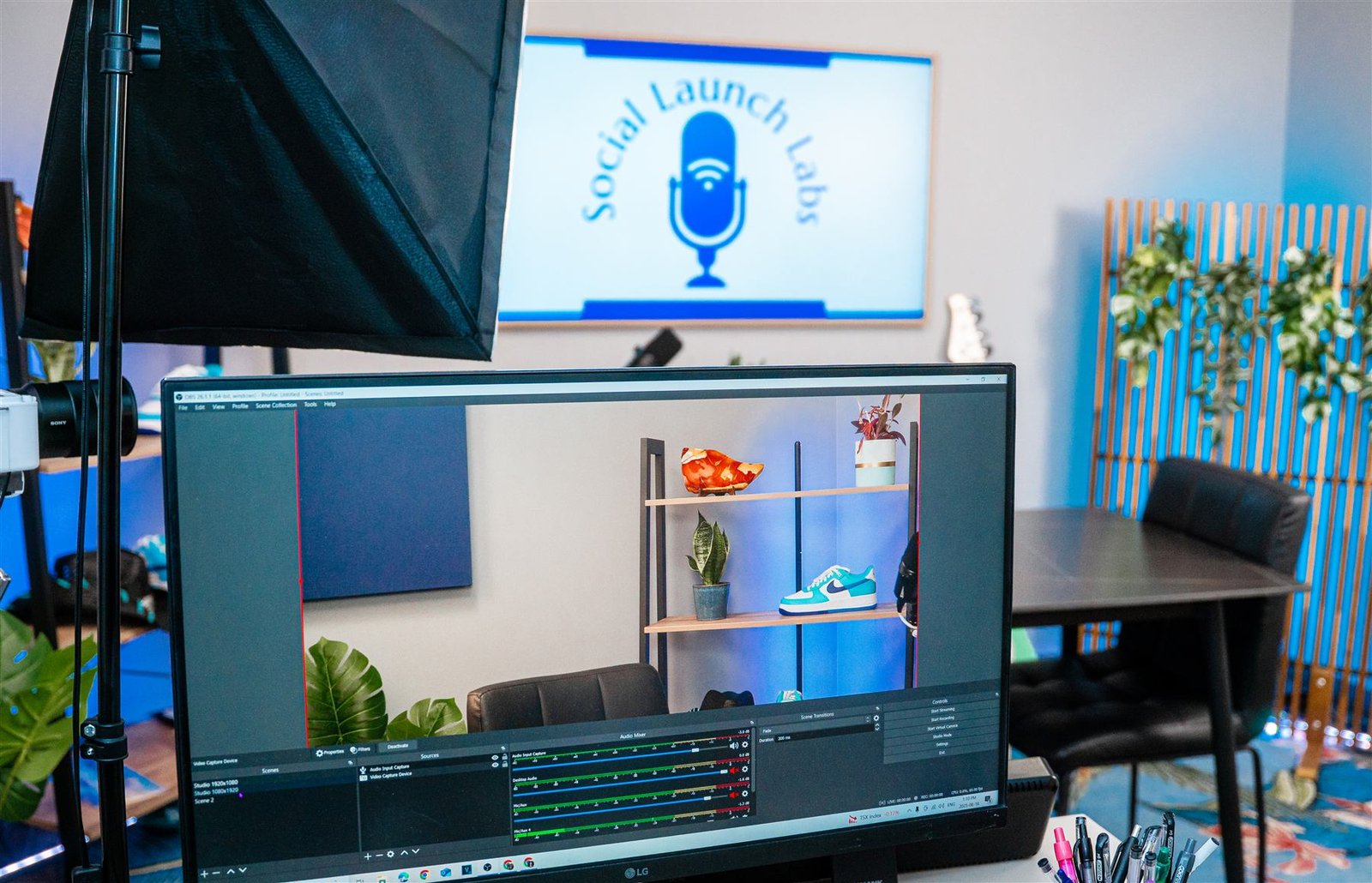 Studio monitor showing a live OBS recording scene, with professional lighting and a shelf styled with plants and sneakers in the background